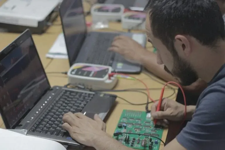 Técnico trabajando en una tarjeta electrónica de un módulo con laptop y equipo de programación